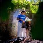 Alex-Mari Ford在院子里铺覆盖物. 她站在篱笆旁边，手里拿着一袋护根物.